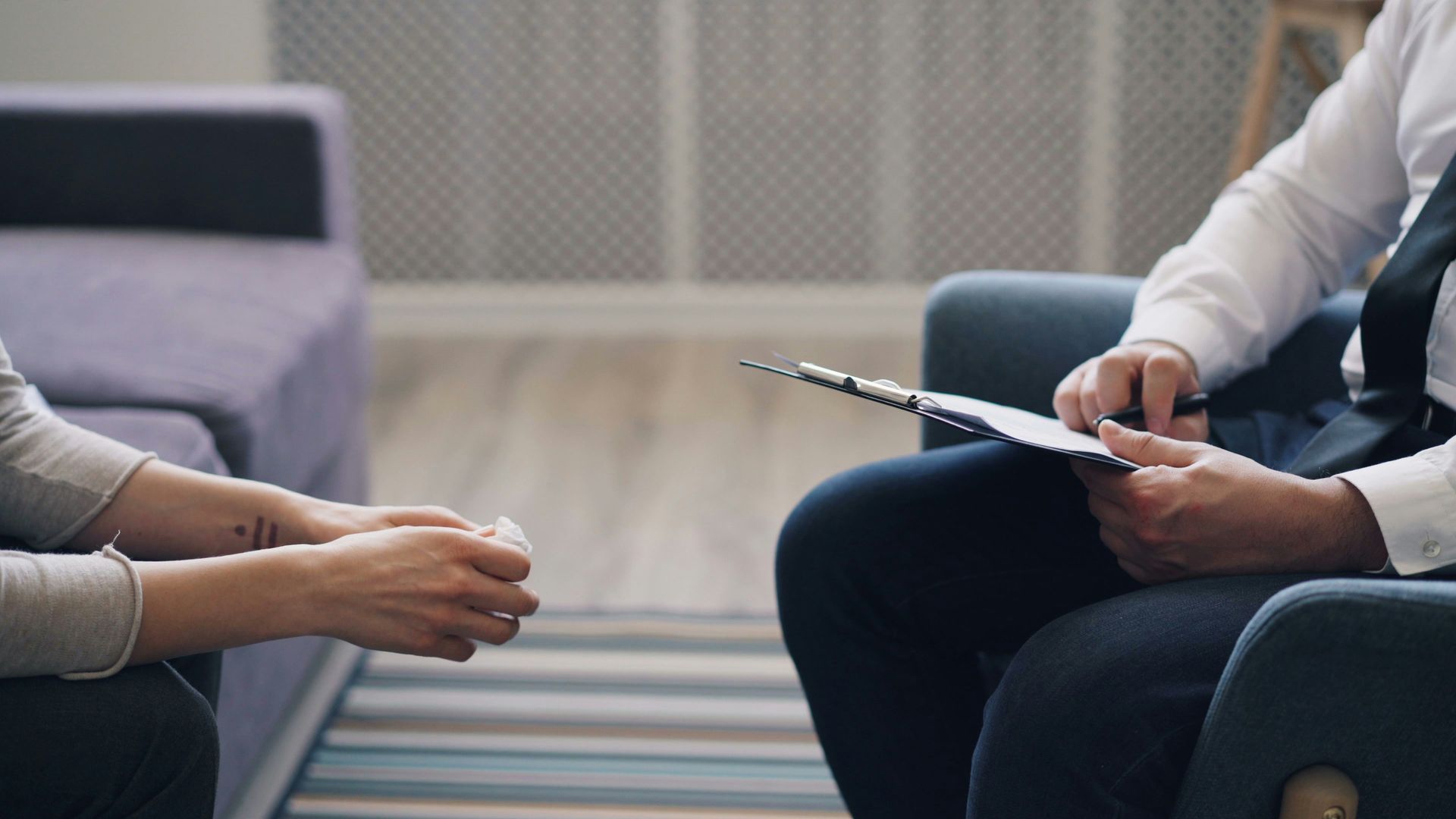 A person holding a tissue facing another person with a clipboard in a room